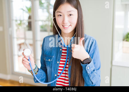 Schöne asiatische Frau prüfen health care mit Stethoskop mit Lächeln tun ok Zeichen glücklich, Daumen hoch, mit den Fingern, ausgezeichnete Zeichen Stockfoto