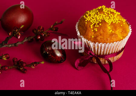 Ostern Muffin mit Schleife dekoriert und besprüht, gefärbte Eier und ein Zweig der Aprikosenbaum auf dunklem Rosa oder Pink Hintergrund. Kopieren Sie Platz. Greetin Stockfoto