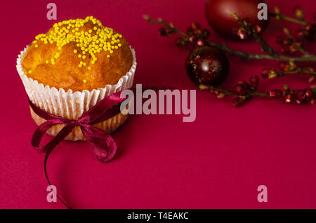 Ostern Muffin mit Schleife dekoriert und besprüht, gefärbte Eier und ein Zweig der Aprikosenbaum auf dunklem Rosa oder Pink Hintergrund. Kopieren Sie Platz. Greetin Stockfoto