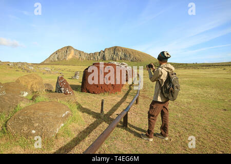 Mann Fotografieren der oberen Knoten oder Hut von Moai Statue Anzeigen auf dem Boden am Ahu Tongariki, archäologische Stätte in Easter Island, Chile Stockfoto