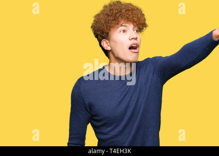 Junger stattlicher Mann mit afro Haar zeigte mit dem Finger vor überrascht, offenem Mund erstaunt Ausdruck, etwas vor Stockfoto