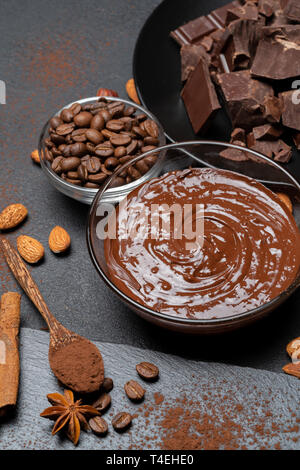 Geschmolzene Schokolade oder Haselnuss Verbreitung in Glasschale und Schokolade Stücke auf dunklen konkreten Hintergrund Stockfoto