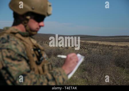 Ein US-Marine mit speziellen Zweck Marine Air-Ground Task Force-Crisis Response-Africa 19.1, Marine Kräfte in Europa und in Afrika, wirkt als Position der Sicherheitsbeauftragte für die Soldaten der 12. der georgischen Armee Infanterie Bataillon, und Soldaten der 3. der moldawischen Armee Infanterie Brigade, bei der abschließenden Übung Teil der Platinum Eagle 19.1, eine multilaterale Übung am Babadag, Rumänien statt, 19. März 2019. SPMAGTF-CR-AF ist eingesetzt Krise - Reaktion und Theater zu leiten - Security Operations in Afrika und die Förderung der regionalen Stabilität durch die Durchführung von militärischen Ausbildung ueb Stockfoto