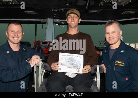 U.S. Navy Aviation Elektriker Mate's Flieger Jared Hammond, von Buena Park, Kalifornien, posiert für ein Foto wie die Segler des Tages mit Kapitän Randy Peck, rechts, kommandierender Offizier der Flugzeugträger USS John C Stennis (CVN 74) und Command Master Chief Benjamin Hetzen in den Arabischen Golf, 3. April 2019. Die John C Stennis Carrier Strike Group ist in die USA 5 Flotte Bereich der Maßnahmen zur Unterstützung der Marine im Einsatz für die Stabilität und Sicherheit in der Region zu gewährleisten und verbindet das Mittelmeer und den Pazifischen Raum durch den westlichen Indischen Ozean und drei Stra Stockfoto