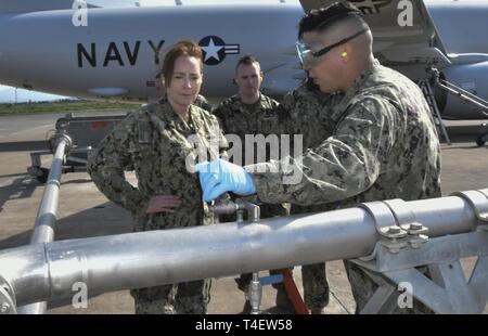 Naval Supply System Befehl (NAVSUP) Commander RADM Michelle Skubic hört wie der Luftfahrt Bootsmann Mate Kraftstoffe 2. Klasse Albert Rodriguez, navsup Flotte Logistikzentrum Sigonella Der Bauernhof Abschnitt Führer, die Hydro System Kapazitäten des Stromabnehmers direkte kraftstoffzufuhrsystems erklärt März 26, 2019 auf dem Flug Linie der Naval Air Station Sigonella, Sizilien, Italien. Von Kraftstoffen die Spaltung der NAVSUP FLC verwendet, muss der Stromabnehmer ermöglicht mission Bereitschaft durch die Betankung Spezialisten eine sichere und effiziente Methode der Reaktion auf große Treibstoff für Flugzeuge, die auf dem Flug. Stockfoto