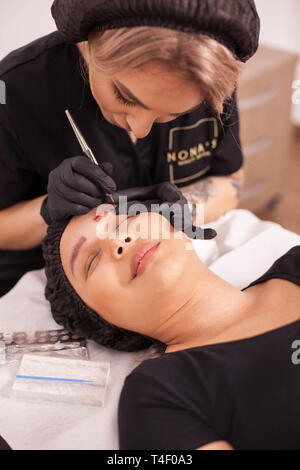 Weibliche Kosmetikerin entfernen Augenbraue Tattoo mit modernen techonolgy in Ihren Salon. Pflege der Haut. Mädchen Patienten. Tattoo Entfernung. Stockfoto