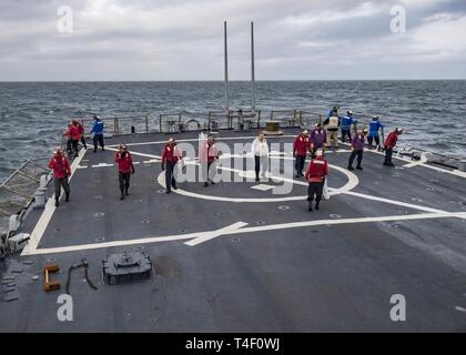 Ozean (April 7, 2019) - Matrosen an Bord der Arleigh-Burke-Klasse geführte Anti-raketen-Zerstörer USS Carney (DDG64) die Flight Deck für den Flugbetrieb vorbereiten, während der übung Gemeinsame Krieger 19-1, 7. April 2019. Gemeinsame Krieger ist ein Vereinigtes Königreich - led, multinationale Übung in einem robusten maritime Ausbildung Umfeld, in dem die Verbündeten und Partnern Interoperabilität verbessern kann und Kräfte für kombinierte Operationen vorzubereiten. Stockfoto