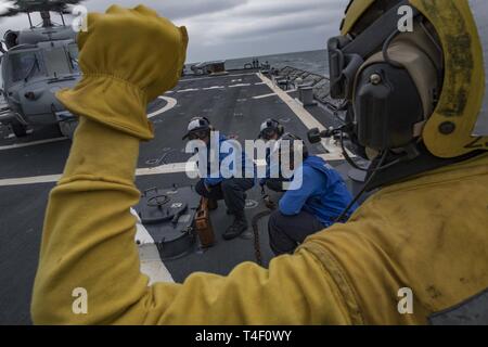 Ozean (April 7, 2019) - eine Gruppe von Matrosen an Bord der Arleigh-Burke-Klasse geführte Anti-raketen-Zerstörer USS Carney (DDG64) Standby für das Signal von der Bootsmann Mate Seemann Chance Vaughn, von Huston, an der Kette, und blockieren Sie einen MH-60S Seahawk, zu der "Ritter" Hubschrauber Meer Combat Squadron (HSC) 22 zugewiesen, während exercsie Gemeinsame Krieger 19-1, 7. April 2019. Gemeinsame Krieger ist ein Vereinigtes Königreich - led, multinationale Übung in einem robusten maritime Ausbildung Umfeld, in dem die Verbündeten und Partnern Interoperabilität verbessern kann und Kräfte für kombinierte Operationen vorzubereiten. Stockfoto