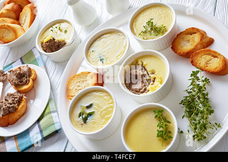 Hausgemachte Leber Pastete mit Kräutern und Butter in Förmchen auf einer Servierplatte mit gerösteten Scheiben Baguette und pastete Leber Sandwiches auf einem Teller, horizontale vi. Stockfoto