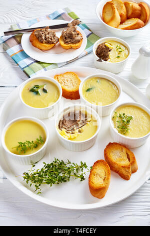 Huhn Leber Pastete mit Kräutern und Butter in Förmchen auf einer Servierplatte mit gerösteten Scheiben Baguette und pastete Leber Sandwiches auf einem Teller, vertikale Ansicht Stockfoto