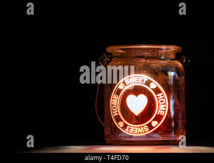 Brennende Kerze Glas mit Sweet Home Inschrift auf schwarzen Hintergrund. Stockfoto