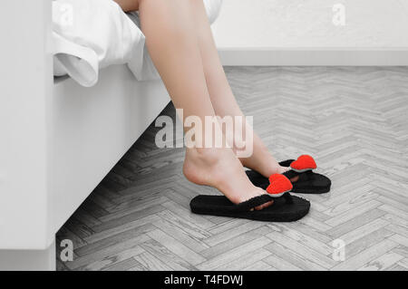 Frauen Füße in Hausschuhen. Das Sitzen auf dem Bett in das Innere des Raumes. Stockfoto