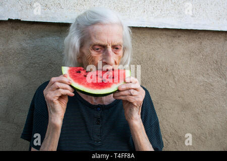 Freundliche Oma essen Wassermelone im Hinterhof Stockfoto