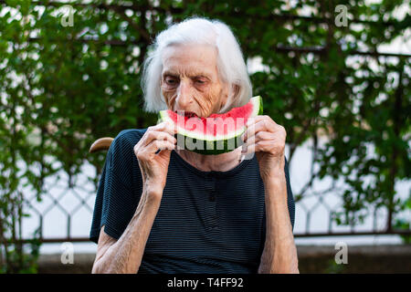 Freundliche Oma essen Wassermelone im Hinterhof Stockfoto