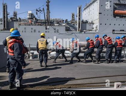 Ozean (10. April 2019) - Matrosen an Bord der Arleigh-Burke-Klasse geführte Anti-raketen-Zerstörer USS Carney (DDG64) während eine Auffüll-anforderung Hebe - auf See - Evolution während der Übung gemeinsame Krieger 19-1, 10. April 2019. Gemeinsame Krieger ist ein Vereinigtes Königreich - led, multinationale Übung in einem robusten maritime Ausbildung Umfeld, in dem die Verbündeten und Partnern Interoperabilität verbessern kann und Kräfte für kombinierte Operationen vorzubereiten. Stockfoto