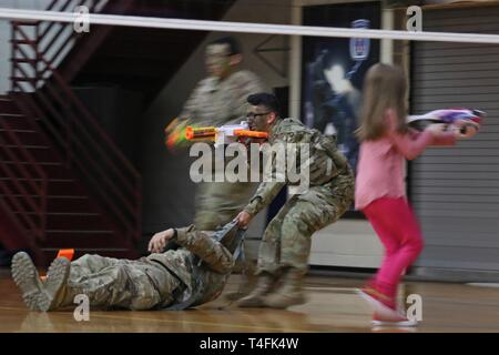 Miniatur Krieger von Familien über 2Nd Brigade Combat Team, 10 Mountain Division, versammelten Soldaten der 41. Engineer Battalion während der Commando Brigade des zweiten 'Nerf Kriege' Match in einem behelfsmäßigen Schlachtfeld statt der gesamten Elze Sports Complex Basketballplatz konfiguriert, 10. April 2019, am Fort Drum, New York. Schaum Dart die Turnhalle während der ÜBERSÄT 'Nur zum Spaß' Ereignis als gegensätzliche Kräfte von Popcorn und Zuckerwatte in einem Spiel Feuergefecht engagiert vorangetrieben. Stockfoto