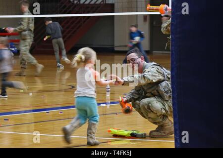 Miniatur Krieger von Familien über 2Nd Brigade Combat Team, 10 Mountain Division, versammelten Soldaten der 41. Engineer Battalion während der Commando Brigade des zweiten 'Nerf Kriege' Match in einem behelfsmäßigen Schlachtfeld statt der gesamten Elze Sports Complex Basketballplatz konfiguriert, 10. April 2019, am Fort Drum, New York. Schaum Dart die Turnhalle während der ÜBERSÄT 'Nur zum Spaß' Ereignis als gegensätzliche Kräfte von Popcorn und Zuckerwatte in einem Spiel Feuergefecht engagiert vorangetrieben. Stockfoto