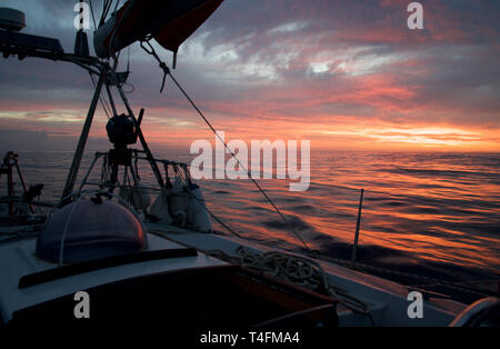 Segeln während eines herrlichen orange, rosa und gelb Sonnenuntergang auf ruhigem Wasser wider Stockfoto