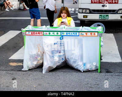 Seoul, Südkorea - 17. Juni 2017: Frau sitzt in der Nähe von abfalltrennung Container mit farbigen Inschriften für Kunststoff, Glas Flaschen und Papier. Stockfoto