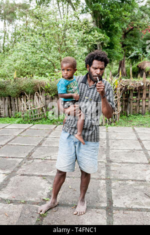 Wamena, Indonesien - Januar 9, 2010: Mann mit Kind der Dani Stamm in einem üblichen Kleidung in Dugum Dani Dorf stehen. Das Baliem Valley in Papua, Irian Jaya Stockfoto