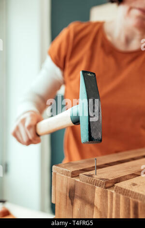 Frau Carpenter Nagel hämmern in Holzkiste in kleinen Unternehmen Holzarbeiten Workshop, selektiver Fokus Stockfoto