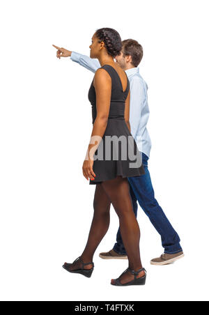 Seitenansicht der interracial, Paar, irgendwo Punkte. zu Fuß freundlich Mädchen und Guy halten sich an den Händen. Ansicht von hinten leute Sammlung. Rückseite Blick auf Stockfoto