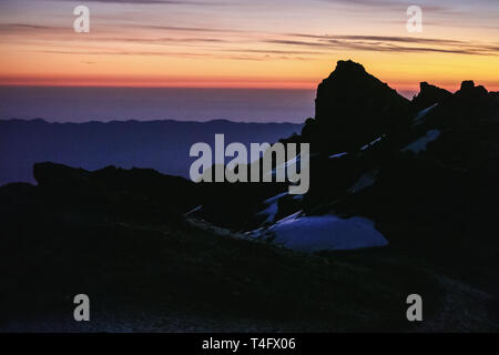 Orange hellen Himmel, herrlicher Panoramablick auf den Sonnenaufgang im afrikanischen Berge. Schwarze Felsen, bedeckt mit Schnee und morgens Nebel. Nach Oben Erhalten Stockfoto