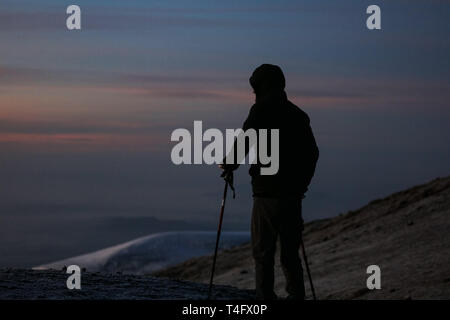 Mann im schwarzen Sportswear steht auf dem Gipfel des Kilimanjaro in Afrika. Genießt die schöne Aussicht auf die Berge auf den Sonnenaufgang. High Peaks Stockfoto