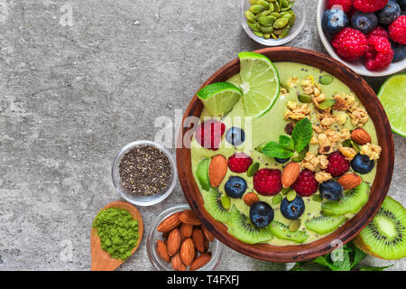 Smoothie Schale aus Matcha grüner Tee mit frischen Früchten, Beeren, Nüsse, Kerne mit einem Löffel für gesunde vegane, vegetarische Ernährung Frühstück. Ansicht von oben mit der Stockfoto