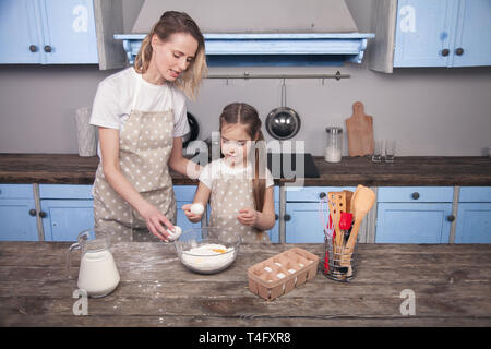 Mutter und Kind Tochter in der Küche zubereiten Teig, Plätzchen backen. Mama lehrt ihre Tochter den Teig aus Mehl, Milch und Eier zu kneten Stockfoto