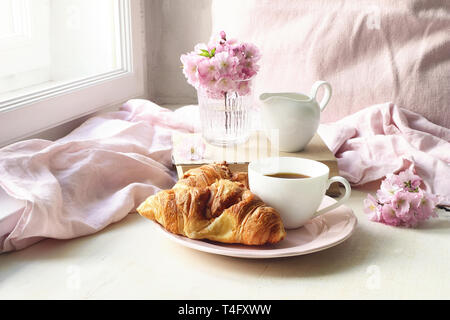 Der Frühling noch leben Szene. Tasse Kaffee, Croissants, Gebäck, alte Bücher und Milch Krug. Vintage feminin Foto, blumige Komposition mit Rosa saku Stockfoto