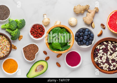 Superfoods auf weißem Marmortisch. Gemüse, Acai, Kurkuma, Früchte, Beeren, Nüsse und Samen. Gesunde vegane Ernährung Top View Stockfoto