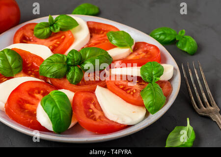 Caprese Salat mit reifen Tomaten und Mozzarella Käse, frische Basilikumblätter auf dunklen konkreten Hintergrund. Italienisches Essen. Nach oben Schließen Stockfoto