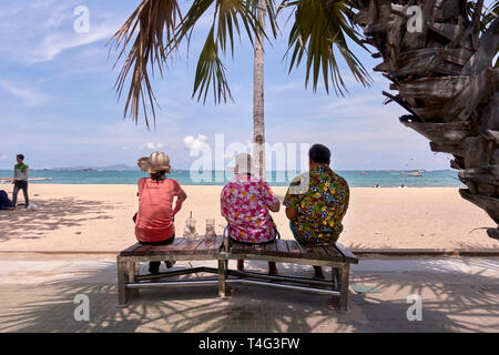 Drei Personen. Mann und zwei Begleiterinnen, die auf einer Bank sitzen und mit Blick auf den Ozean in Pattaya, Thailand, Südostasien Stockfoto