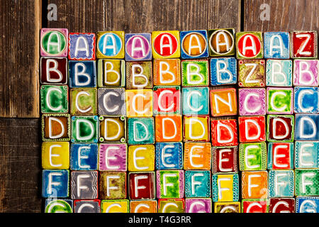 Farbenfrohe handgefertigte Keramik Alphabet auf Holz Textur Stockfoto