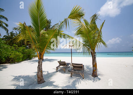 Sonnenschirm und zwei Liegen am Strand mit Sand. Zwei Liegestühle unter Zelt am Strand. Liegestühle, Sonnenschirme und Palmen am Strand Stockfoto