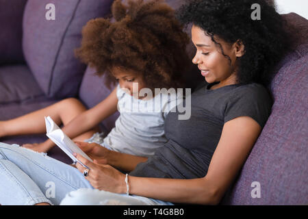 Lächelnd Afrikanische amerikanische Mutter Lesung Buch mit Tochter Stockfoto