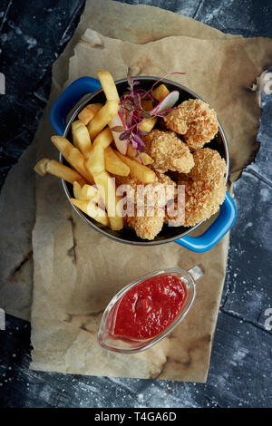 Mittagessen oder einen Snack - Fried Chicken Streifen und Pommes frites in eine Metallwanne mit Tomatensoße. Handwerk Papier im Hintergrund. Stockfoto