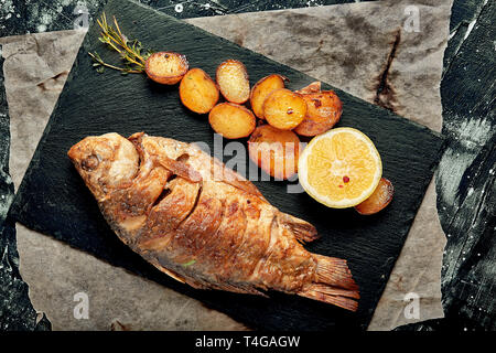 Gegrillter Fisch mit gebackenen Kartoffeln, Zitrone und Soße. Ansicht von oben. Stockfoto