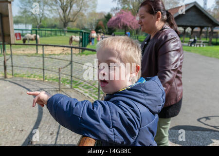 Mangels, Kinderbetreuung, Medizin und Personen Konzept: glückliche Mutter und Sohn mit Down-syndrom spielen zusammen in einem Park im Frühling. Stockfoto