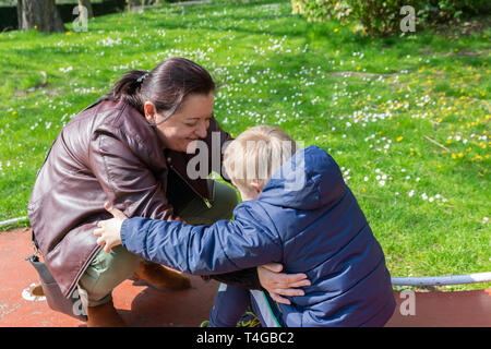 Mangels, Kinderbetreuung, Medizin und Personen Konzept: glückliche Mutter und Sohn mit Down-syndrom spielen zusammen in einem Park im Frühling. Stockfoto