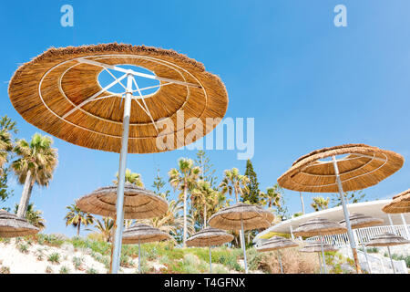 Reed Strand Regenschirme, Sonnenschirme gegen den blauen Himmel am Strand. Bambus Sonnenschirme, Stroh Sonnenschirme am weißen Sandstrand tropischen Meeres. Tropische Meer Stockfoto