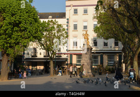 Frühlingssonne genossen die Besucher unter der Statue von König Georg II. in der Royal Square, St Helier, Jersey, Channel Islands Stockfoto