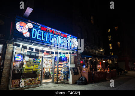New York City, USA - 2. August 2018: Beleuchtetes Display von ein Lebensmittelgeschäft in der Nacht neben einer Terrasse der Bar mit einem Drink auf Sommer in Stockfoto