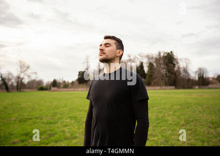 Man entspannen und die frische Luft in einem Stadtpark. schöner Mann tief atmen an einem sonnigen Frühlingstag. Freizeitmöglichkeiten Konzept. Stockfoto