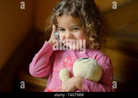 Mädchen, 3 Jahre, Porträt, sitzt lächelnd auf den Treppen mit Handy, rief, Deutschland Stockfoto