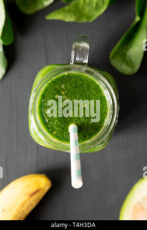 Grüne Smoothie mit Avocado, Spinat und Banane in einem Glas über schwarze Oberfläche, Ansicht von oben. Flach, Ansicht von oben, Overhead. Stockfoto