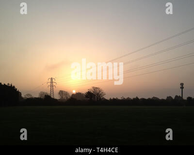 Die aufgehende Sonne in einer semi-ländlichen Umgebung, mit einem Telefon Mast und ein Strom pylon Stockfoto