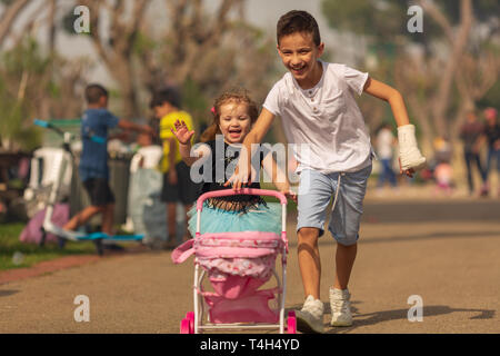 Junge und Mädchen spielen ein Spiel der Kinder beim Spielen in einen Kinderwagen in einem Park. Kinder- Freundschaft. Kinder mit einem Spielzeug Kinderwagen Stockfoto