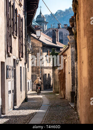 Bild der alte Mann von hinten mit dem Fahrrad durch schmale Straße in einem italienischen Altstadt während des Tages Stockfoto